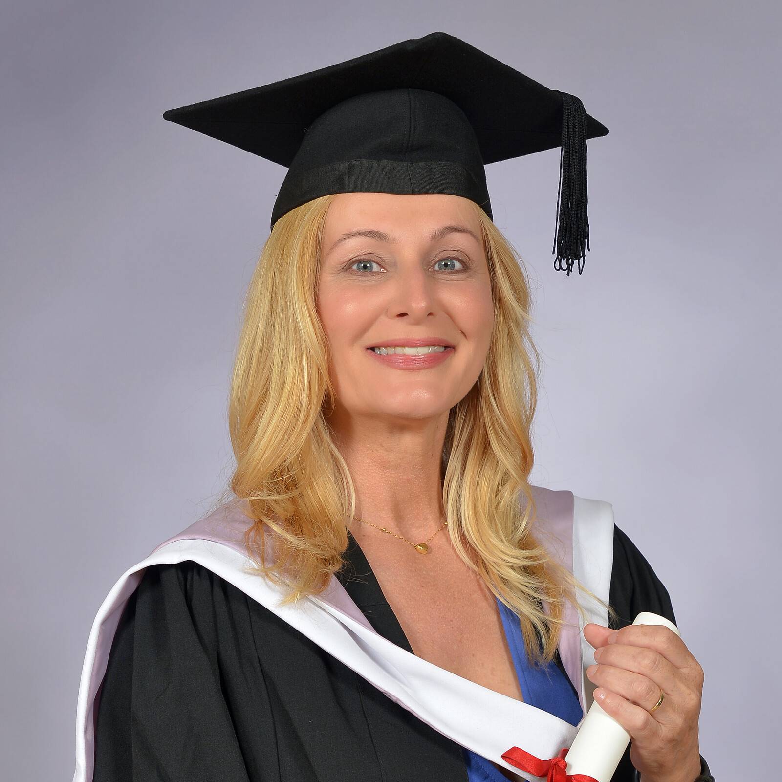 A happy Melpomeni Kavga in graduation robe and cap holds her degree certificate